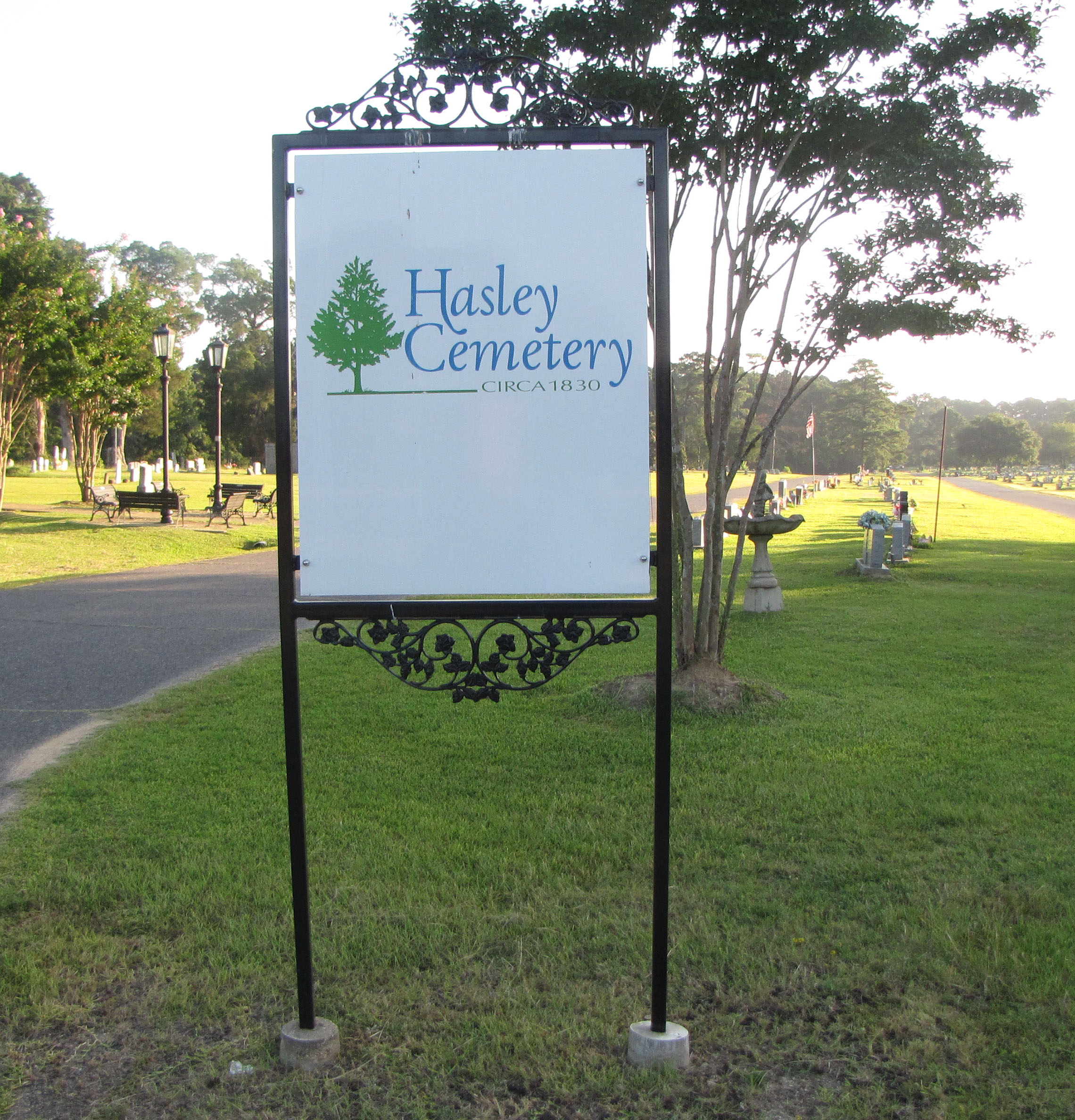 This is the middle main entrance to Hasley Cemetery with a sign on a green lawn.