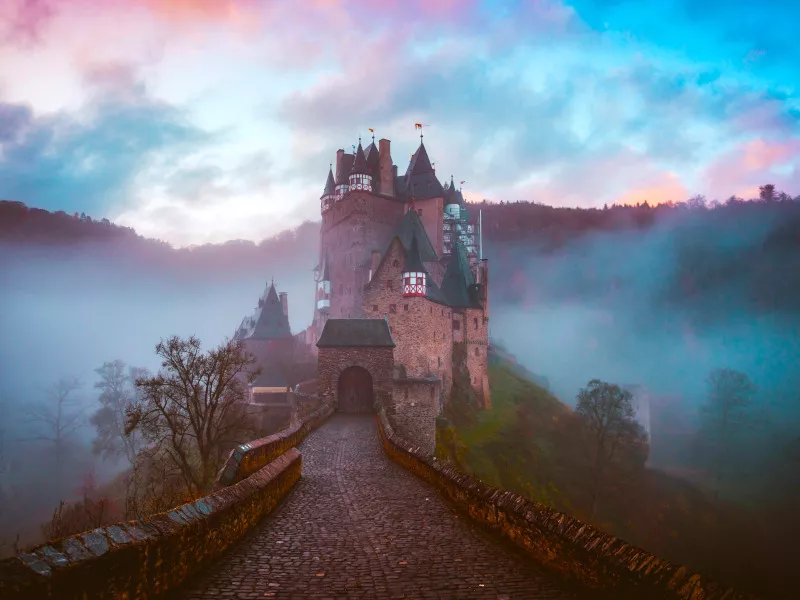 A castle stands at the end of a road beneath a cotton-candy pink and blue sky.