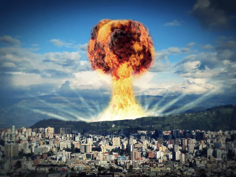 A nuclear bomb explodes behind a foothill. In the foreground stands a densely populated suburb with high-rise residential buildings.