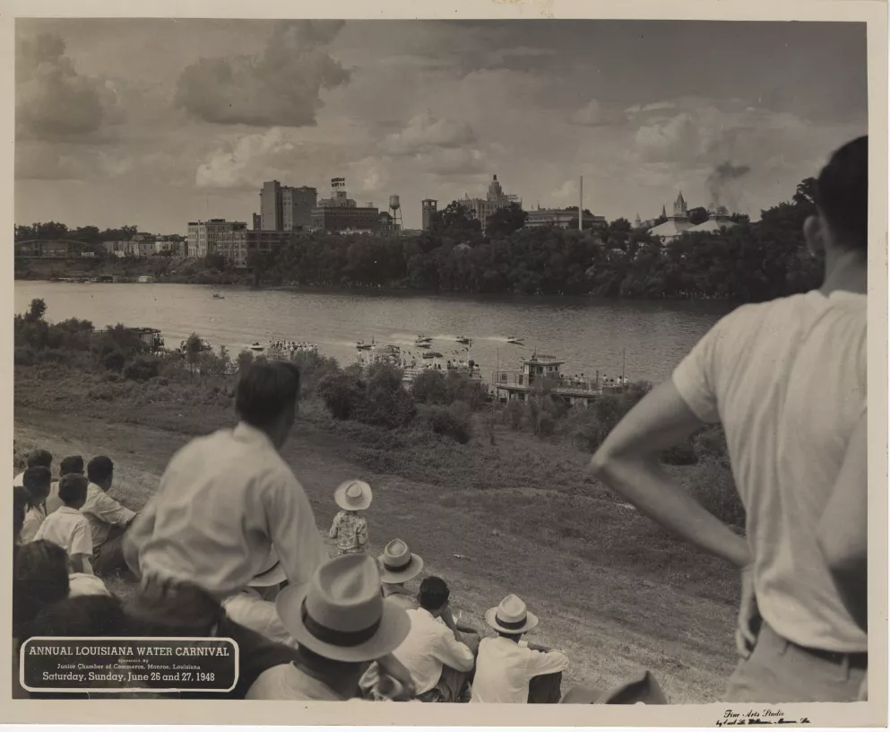 Image from the Louisiana Digital Library, showing a crowd of people on the levee watching boat races on the Ouachita River. The Monroe skyline is in the background.