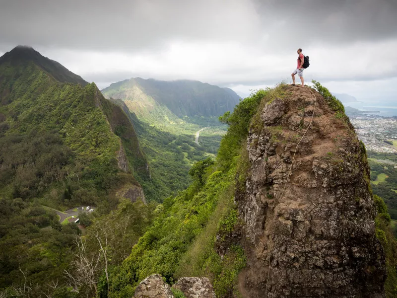 A hiker stands alone on top of the Pali Notches of the Koʻolau Mountain Range