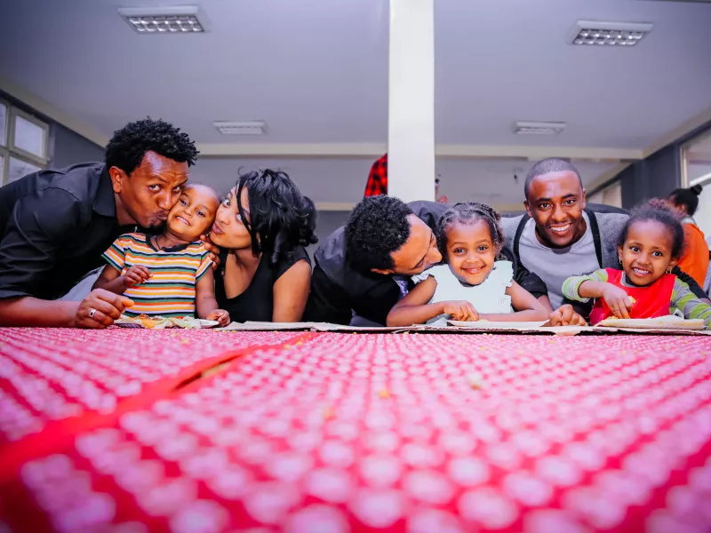 Four adults lean down affectionately to pose with three children in front of a red table.