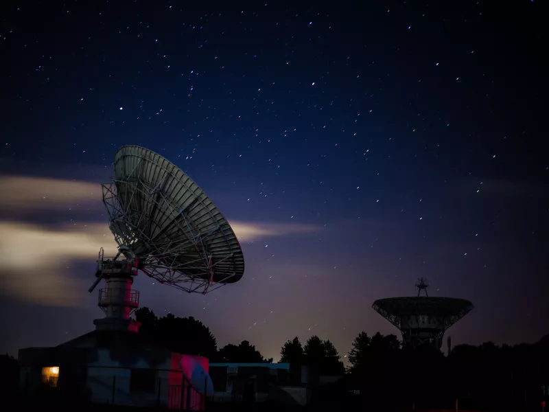 A tilted parabolic antenna listens at dusk to the starry sky above France