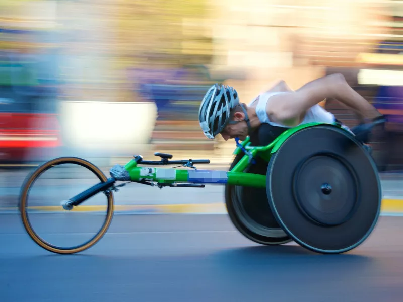 An athlete leans forward in his green racing wheelchair during the 2017 Chicago marathon as the background blurs with his speed